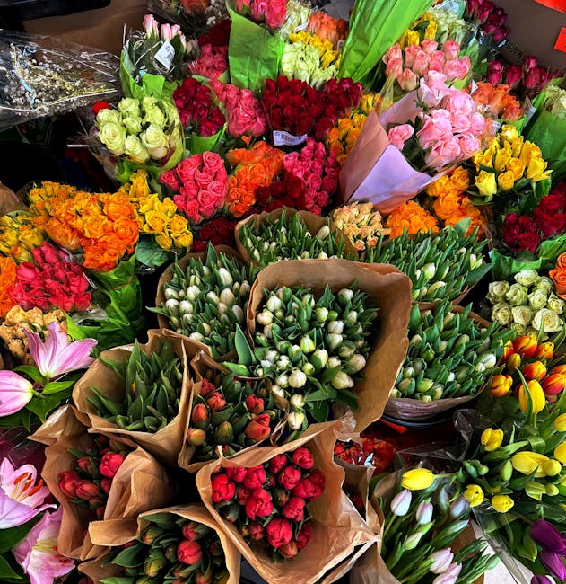 An assortment of fresh flower bouquets arranged closely together, featuring a vibrant variety of blooms. There are traditional roses in shades of pink, red, yellow, and orange, alongside tulips in whi