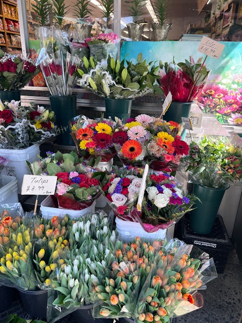 A display of fresh flowers at a florist shop, including colorful bouquets of tulips, daisies, and chrysanthemums. The tulips, in shades of yellow, orange, and white, are wrapped in clear plastic and a