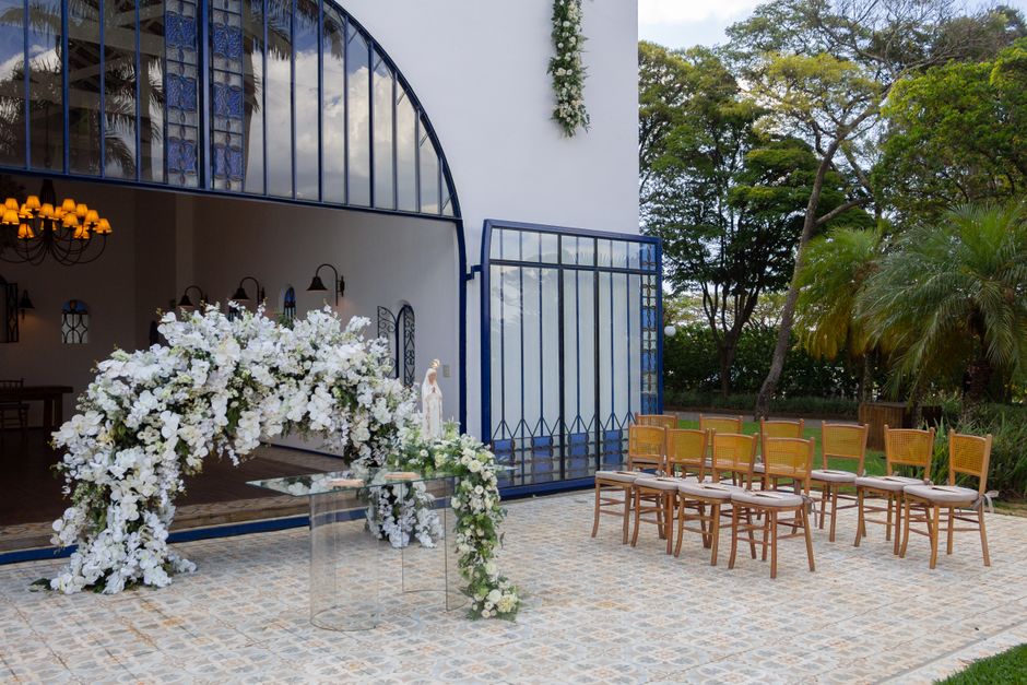 A floral arrangement for a wedding, featuring a large, cascading bouquet predominantly composed of white roses, hydrangeas, and orchids, arranged in an elegant arch shape with lush greenery accents. T