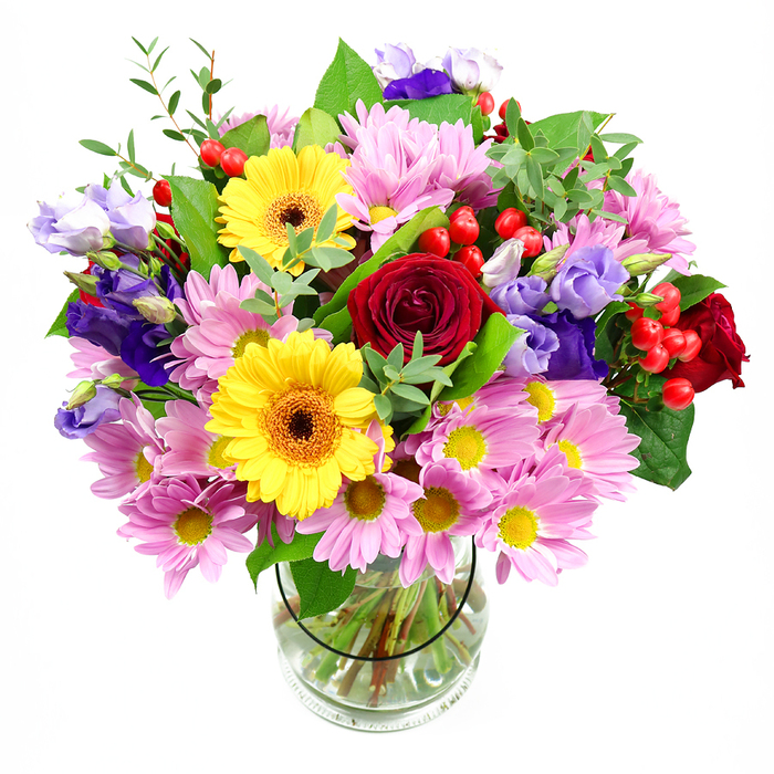 A lavish mixed-colour bouquet rises from a clear glass vase, the flowers arranged with the easy elegance of an experienced local florist. Against a plain white backdrop, the colours appear almost luminous: rich crimson roses unfold at the centre, their velvety petals suggesting a classic, heartfelt sentiment. Just off centre, vibrant yellow gerbera daisies with dark brown-orange centres bring a lively, almost sunlit energy to the design, creating a striking contrast with the roses. Encircling this core are generous clusters of pink and soft lavender daisies or chrysanthemums, each flower made up of many slim petals radiating from a small yellow centre, adding both volume and a cosy, familiar charm reminiscent of cottage gardens near Elm Park station. Threads of lisianthus in shades of purple and pale lilac wind through the bouquet, some blooms trumpet-shaped and open, others still in graceful buds, contributing a sense of layered depth and quiet sophistication. Bright red hypericum berries, smooth and round, peek out from between the petals, punctuating the arrangement with playful pops of colour and tactile interest. The flowers are supported by a collar of varied greenery, from glossy, broad leaves to lighter, more delicate sprigs that give the bouquet its full, rounded silhouette and a freshly gathered feel. Through the sides of the glass vase, you can see the stems neatly cut and arranged in clear water, evidence of careful preparation and attention to detail. This mixed arrangement radiates warmth and celebration, ideal as a thoughtful delivery for birthdays, housewarmings, or simply to lift the mood in an Elm Park home on an overcast afternoon.